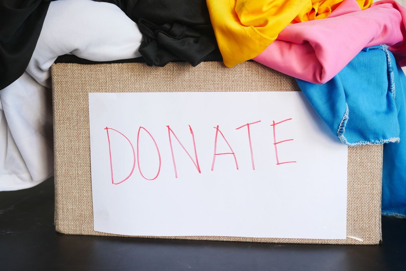 A woven donation box filled with folded clothes in different colours